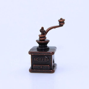 May include: A miniature antique-style coffee grinder with a copper finish. The grinder has a crank handle and a drawer labeled "CAFE".