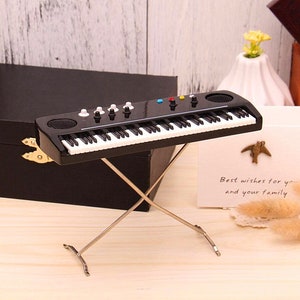 May include: A small black keyboard with white keys and coloured buttons on a silver stand. The keyboard is in front of a black box and a card that reads "Best wishes for you and your family."