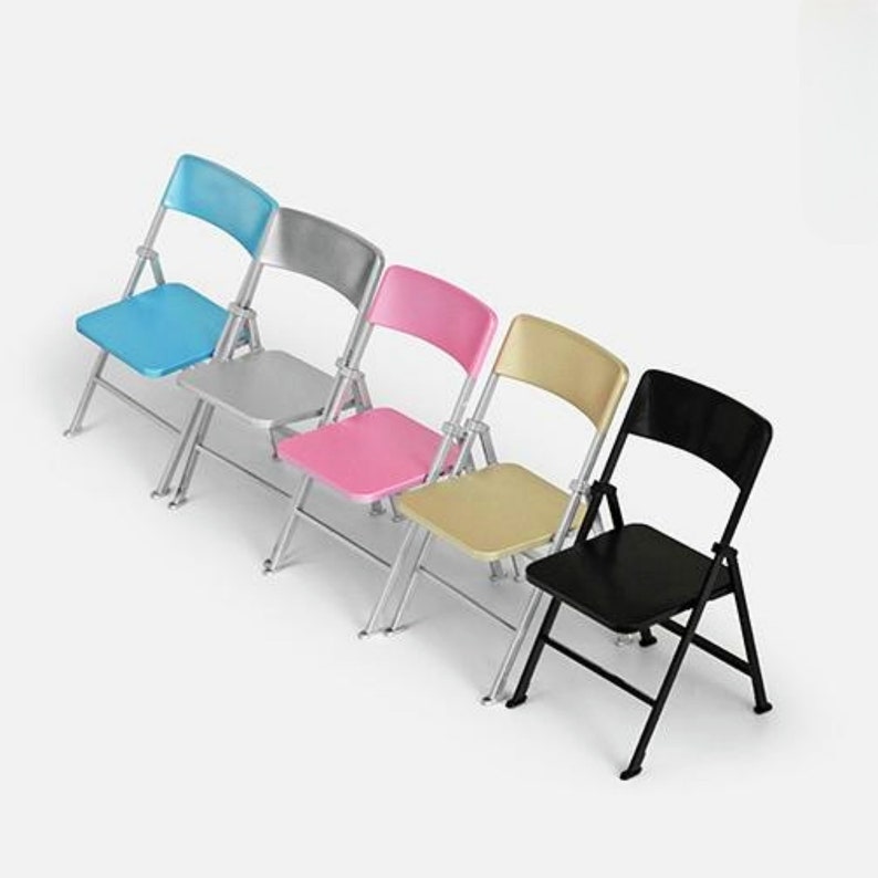 May include: Five folding chairs in different colors: blue, silver, pink, gold, and black. The chairs are made of metal and have a simple design.