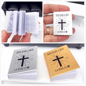 Puede incluir: Dos r&eacute;plicas de la Biblia en miniatura, una plateada y otra dorada, con el texto "DIOS HABLA HOY" y "LA BIBLIA+". Las cubiertas presentan una cruz negra con un dise&ntilde;o de sol.