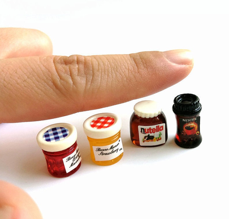 May include: Four miniature glass jars with lids. The jars contain red, yellow, brown, and black substances. The jars are labeled "Bonne Maman Strawberry", "Nutella", and "Nescafe".