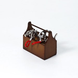 May include: A brown wooden toolbox with a metal handle and various tools inside, including a pair of red-handled scissors, a metal nutcracker, and a metal tool with a red handle.