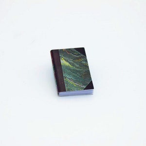 May include: A small, closed book with a dark green and brown marbled cover. The book is closed and the spine is visible.