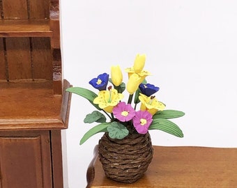 Puede incluir: Un arreglo floral en miniatura en una cesta tejida marrón. Las flores son amarillas, rosas y azules.