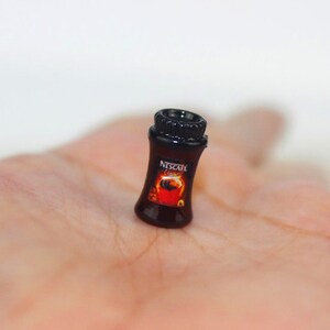 May include: A miniature black plastic jar with a red and orange label that says "Nescafe Classic".