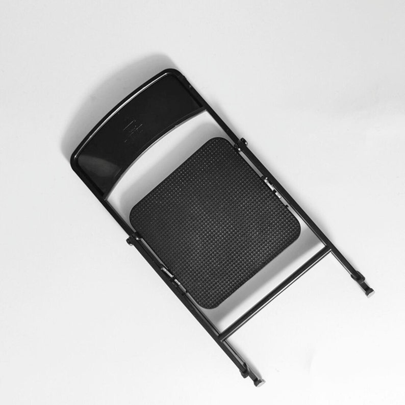 May include: A black folding chair with a textured seat. The chair is folded and the seat is facing up.