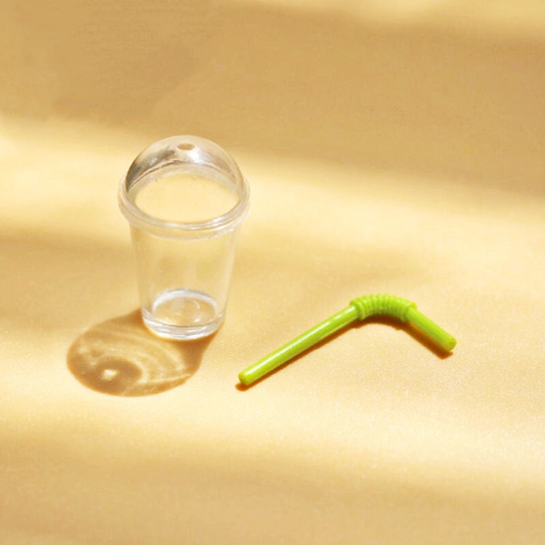 Puede incluir: Un vaso de pl&aacute;stico transparente con tapa y una pajita de pl&aacute;stico verde. El vaso y la pajita est&aacute;n sobre una superficie marr&oacute;n claro.