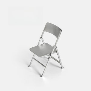 May include: A silver folding chair with a textured seat and back. The chair is made of metal and has a simple design.