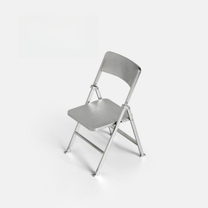 May include: A silver folding chair with a textured seat and back. The chair is made of metal and has a simple design.