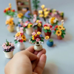 May include: A collection of miniature handmade flower arrangements in small vases and pots. The arrangements feature colourful flowers in shades of red, yellow, pink, and blue. Some are in ceramic vases, others in woven baskets or terracotta pots.