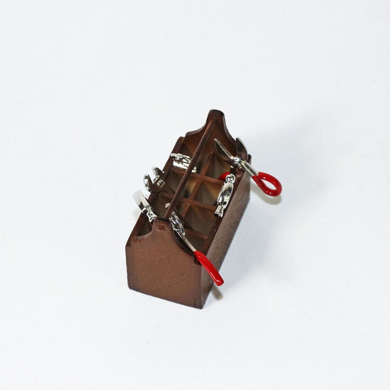 May include: A miniature wooden toolbox with a brown finish and a variety of small tools, including a wrench, pliers, and a screwdriver. The tools are arranged in the compartments of the toolbox.