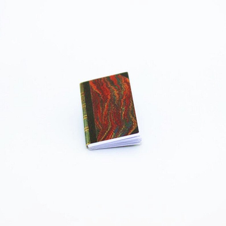 May include: A small, closed book with a red, orange, and green marbled cover. The book is closed and lying flat on a white surface.