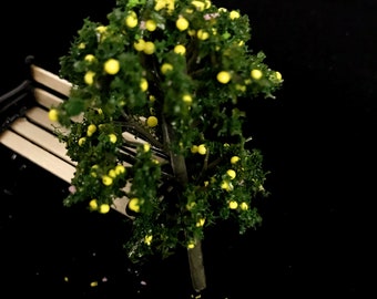 Op de afbeelding: Een miniatuurmodel van een boom met groene bladeren en gele vruchten. De boom staat op een houten bank.