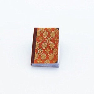 May include: A small, orange and gold patterned book with a brown spine.