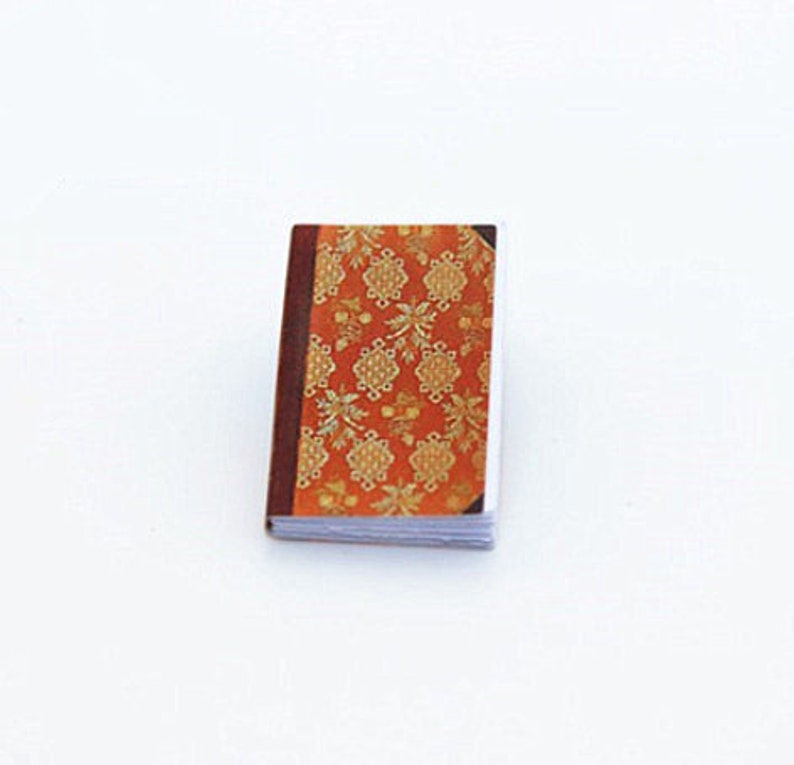 May include: A small, orange and gold patterned book with a brown spine.