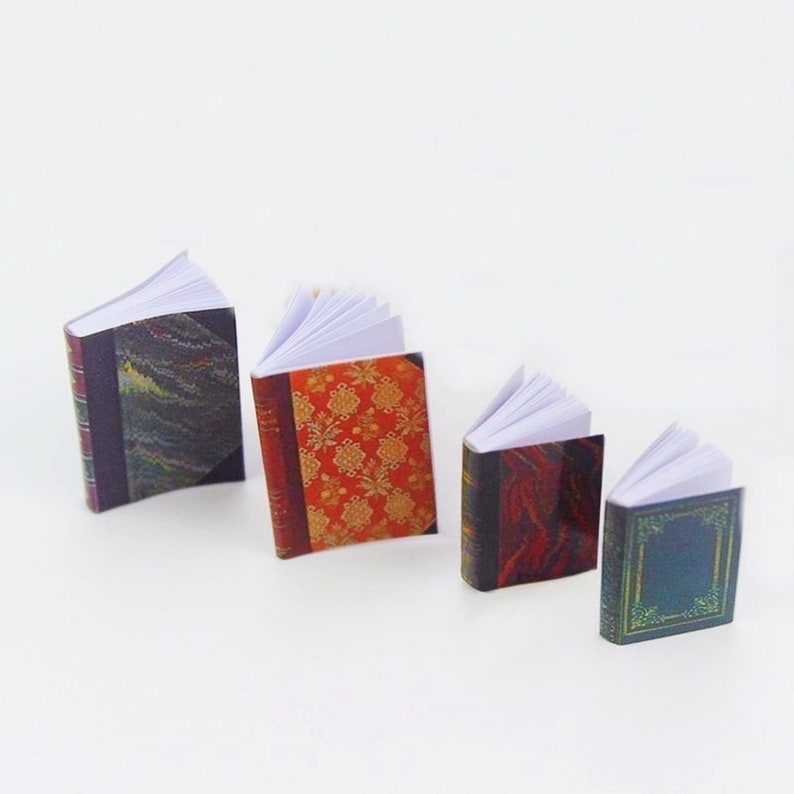 May include: Four miniature books with different patterned covers. The books are open and have white pages. The covers are a mix of red, green, black, and gold.