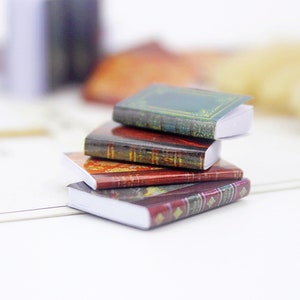 May include: A stack of four miniature books with decorative covers. The top book has a green cover with gold accents, the second book has a red and gold cover, the third book has a red and gold cover with a plaid pattern, and the bottom book has a red and gold cover with a floral pattern.