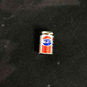 May include: A miniature silver can with a red, white, and blue label that says "Soda Pop".