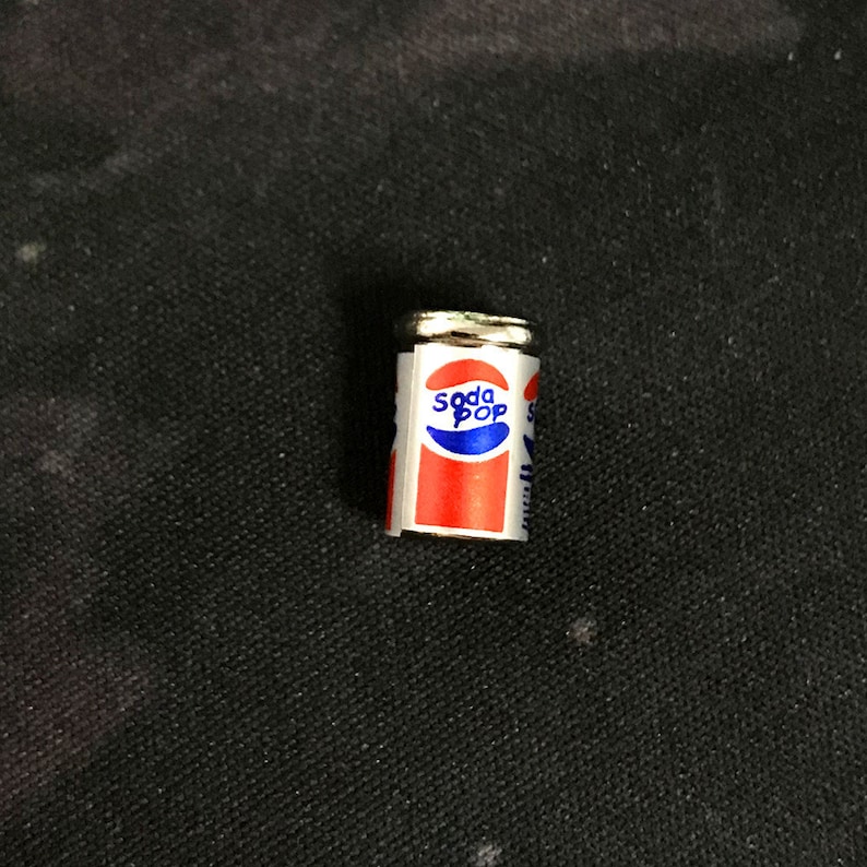 May include: A miniature silver can with a red, white, and blue label that says "Soda Pop".