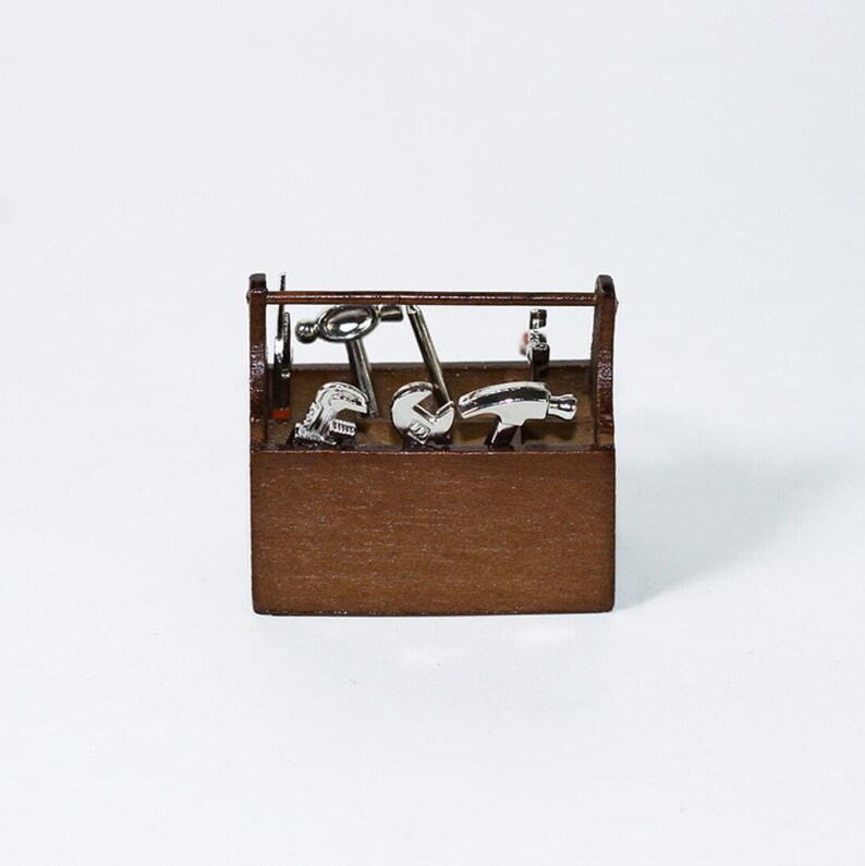 May include: A small wooden toolbox with a hinged lid, filled with miniature tools, including a hammer, wrench, and screwdriver. The tools are made of silver metal.