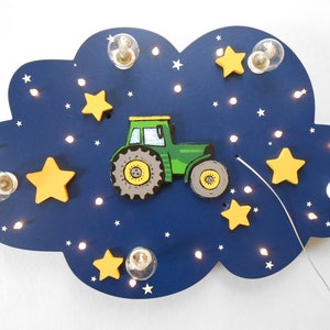 Könnte beinhalten: Eine blaue, wolkenförmige Nachtlampe aus Holz mit einem grünen Traktor und gelben Sternen. Die Wolke hat eine Lichterkette aus weißen Lichtern am Rand und mehrere kleine weiße Lichter im Inneren der Wolke.