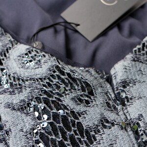May include: Close-up of a gray and black sequined top. The fabric has a textured pattern with silver sequins. A gray tag hangs from the garment. The top is likely part of a formal wear collection.