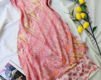 May include: A sleeveless slip dress featuring a vibrant pink and yellow patterned print with intricate geometric and floral motifs. The dress has thin adjustable shoulder straps, a scoop neckline, and a layered hemline with a contrasting floral pattern.