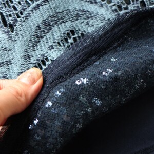 May include: Close-up of a dark blue fabric with a layered design. The top layer is a delicate, open-weave lace, while the bottom layer appears to be a solid, opaque material. The edges are neatly sewn together.