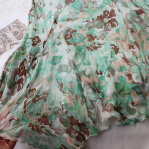 May include: A flowing, sheer fabric with a floral pattern in shades of green, brown, and peach. The fabric is draped over an open book, with the edges of the fabric slightly ruffled. The overall effect is soft and delicate.