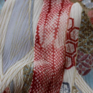 May include: Close-up of a patterned fabric with a mix of colors. The design features red, white, and blue sections with geometric and floral patterns. The fabric has a textured appearance, with visible threads and subtle variations in color.