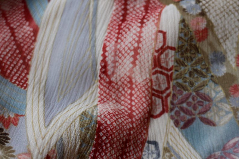 May include: Close-up of a patterned fabric with a mix of colors. The design features red, white, and blue sections with geometric and floral patterns. The fabric has a textured appearance, with visible threads and subtle variations in color.