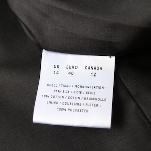 May include: Close-up of a garment label with size information for UK, Euro, and Canada. The label lists the shell fabric composition as 81% silk and 19% cotton, with a 100% polyester lining. The label is white with black text.