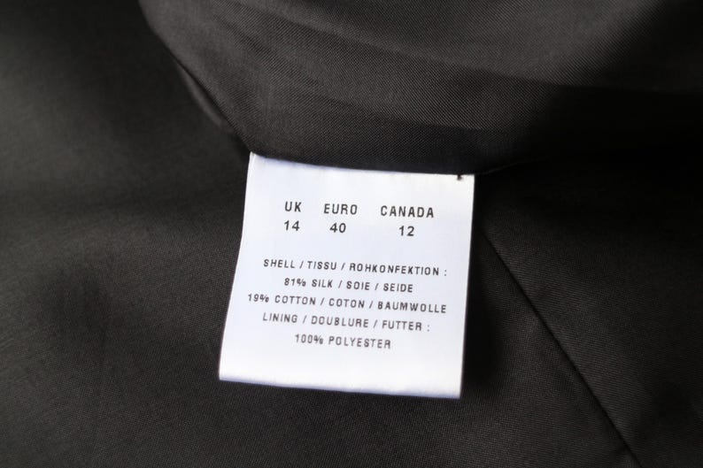 May include: Close-up of a garment label with size information for UK, Euro, and Canada. The label lists the shell fabric composition as 81% silk and 19% cotton, with a 100% polyester lining. The label is white with black text.