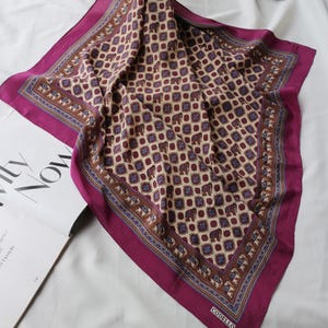 May include: A square silk scarf with a repeating elephant pattern in burgundy, brown, and blue on a beige background. The scarf has a deep magenta border and the brand name "CODELLO" is visible.