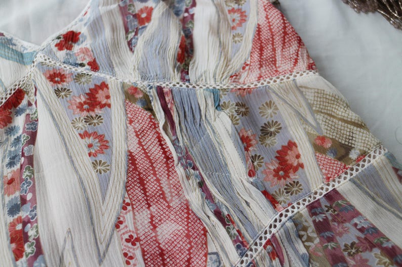 May include: Close-up of a patchwork fabric with floral and geometric patterns. The fabric features a mix of red, blue, and white hues, with delicate lace trim. The design includes stripes and floral motifs, creating a textured, layered effect.