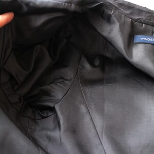 May include: Close-up of the inside of a dark gray jacket. The lining is a darker shade of gray and appears smooth. A small blue tag with the text "WINDSMOOR" is visible.