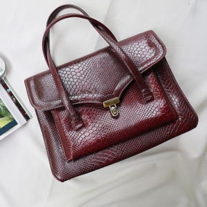Bolso tote estructurado de piel vintage con estampado de serpiente, color burdeos y cierre dorado, estilo años 80.