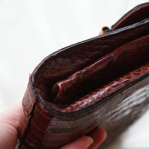May include: A close-up of a brown leather wallet with a textured exterior. The wallet has a dark brown interior and a gold-colored clasp. The wallet appears to be vintage.