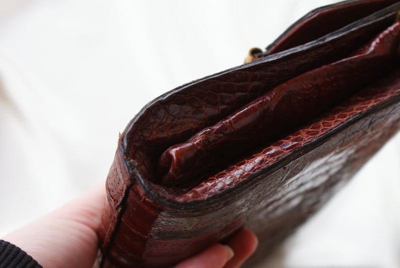 May include: A close-up of a brown leather wallet with a textured exterior. The wallet has a dark brown interior and a gold-colored clasp. The wallet appears to be vintage.