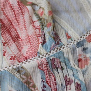 May include: Close-up of a patterned fabric with a mix of floral and geometric designs. The fabric features a color palette of red, blue, and cream, with delicate lace trim. The overall aesthetic is soft and feminine.