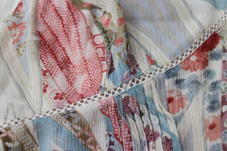 May include: Close-up of a patterned fabric with a mix of floral and geometric designs. The fabric features a color palette of red, blue, and cream, with delicate lace trim. The overall aesthetic is soft and feminine.