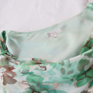 May include: A light green and brown floral print dress. The dress features a one-shoulder design with a flowing, lightweight fabric. The inner lining is a solid light green color. The dress has a tag with the letters "jc".