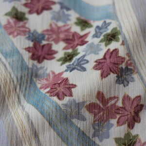 May include: Close-up of a fabric with a floral pattern. The fabric has a cream background with vertical stripes in light brown and blue. The floral pattern features pink, blue, and green flowers.