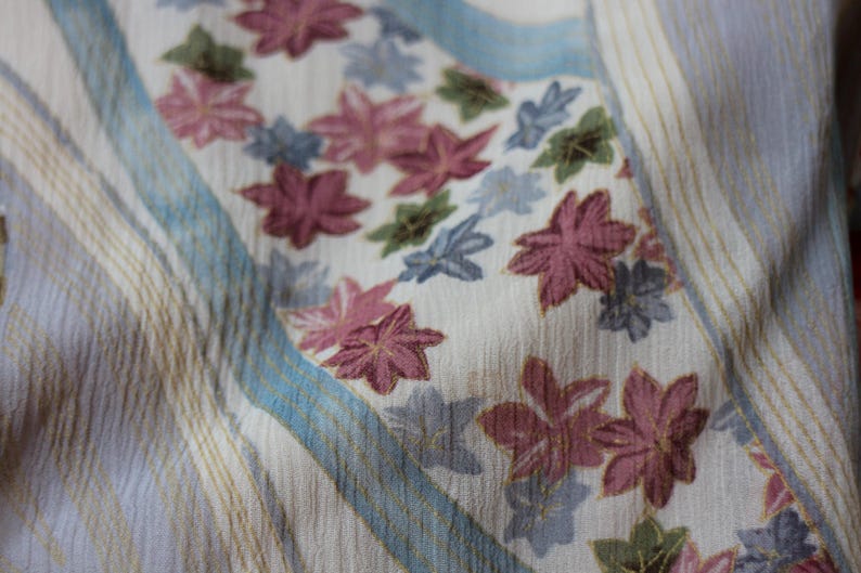 May include: Close-up of a fabric with a floral pattern. The fabric has a cream background with vertical stripes in light brown and blue. The floral pattern features pink, blue, and green flowers.