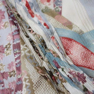 May include: Close-up of a patterned fabric with a variety of designs and colors. The fabric features floral and geometric patterns in shades of pink, blue, and beige. The fabric is draped, creating folds and texture.