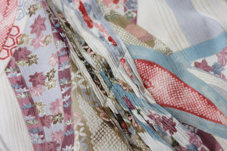 May include: Close-up of a patterned fabric with a variety of designs and colors. The fabric features floral and geometric patterns in shades of pink, blue, and beige. The fabric is draped, creating folds and texture.