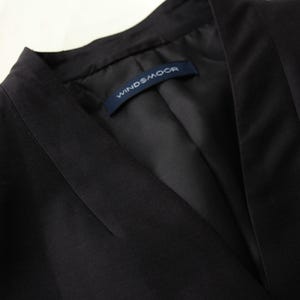 May include: Close-up of a black blazer with a V-neck collar. The blazer has a tailored fit and a label that reads "WINDSMOOR". The fabric appears to be a smooth, dark material.