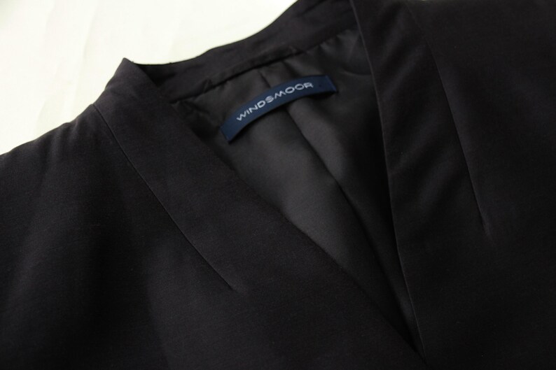 May include: Close-up of a black blazer with a V-neck collar. The blazer has a tailored fit and a label that reads "WINDSMOOR". The fabric appears to be a smooth, dark material.