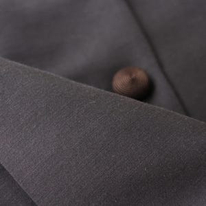 May include: Close-up of dark gray fabric with a brown button. The fabric appears to be a woven material, possibly part of a garment. The button is round and has a textured surface.