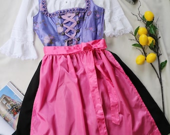 May include: A traditional dirndl dress with a lilac bodice, floral embroidery, and a pink ribbon corset. The dress features a pink skirt with a black hem and a white blouse with lace sleeves. A vintage camera and lemons are also in the image.